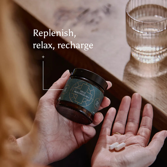 Person holding a container of True Magnesium supplements with text 'Replenish, relax, recharge' on a kitchen table background