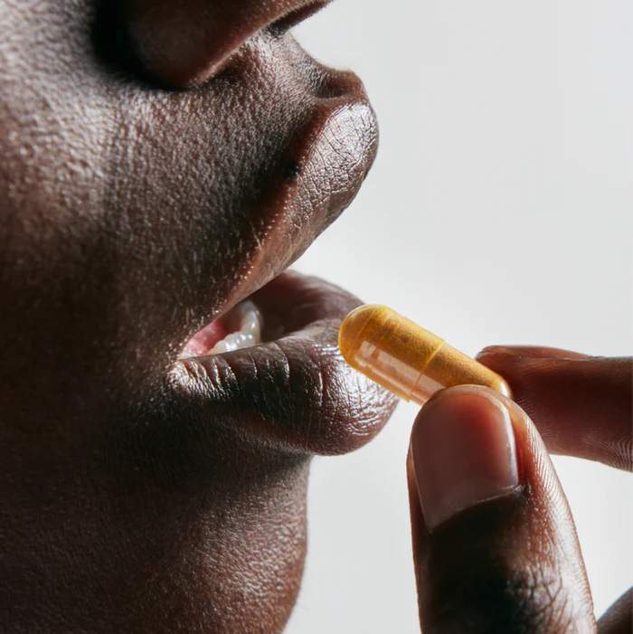 Close-up of a beautiful woman about to take an orange color capsule pill of Neutrient Curcumi