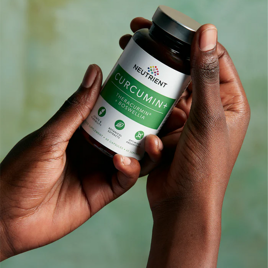 Two elegant female hands holding Neutrient Curcumin supplement bottle against a blurred green background