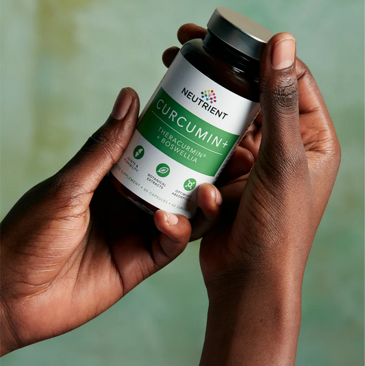 Two elegant female hands holding Neutrient Curcumin supplement bottle against a blurred green background